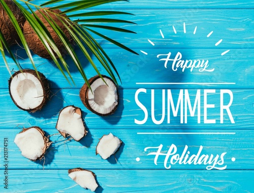 top view of coconuts and green palm leaves on turquoise wooden surface with "happy summer holidays" lettering