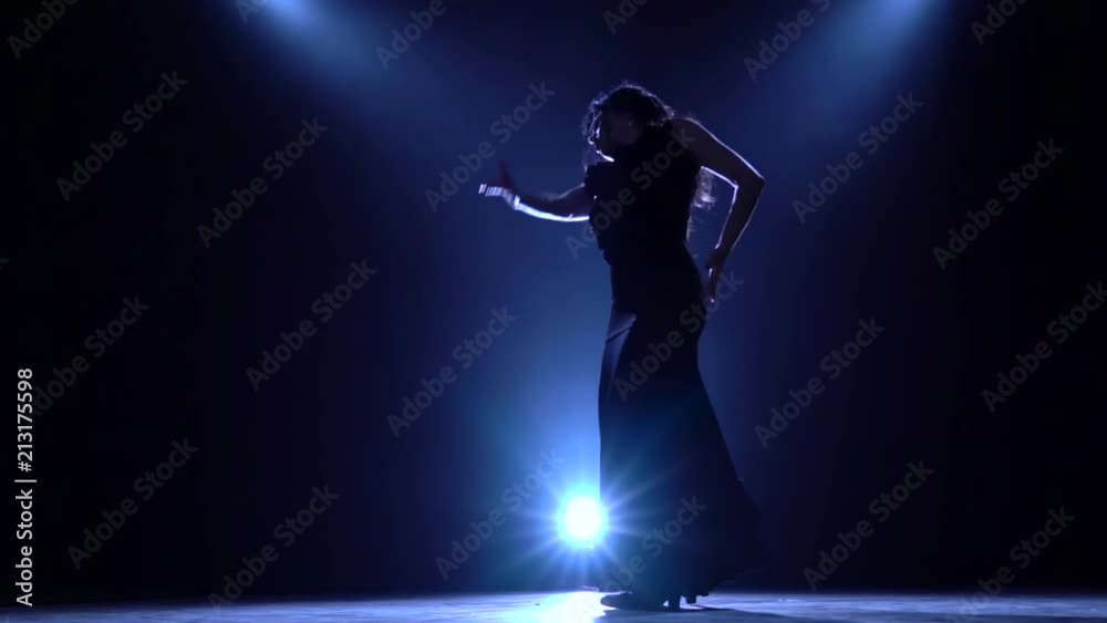 Girl is dancing in a dark room with graceful hand movements. Llight from behind. Smoke background. Silhouette. Slow motion Girl is dancing in a dark room with graceful hand movements. Llight from behind. Smoke background. Silhouette. Slow motion