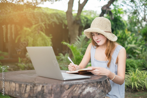 Young cute brown hair woman wearing cream hat using laptop notebook for education and writing text in a park, Technology social media concept.