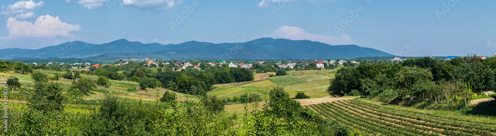 A panorama of hills with agricultural land near the village on the background of the distant mountains