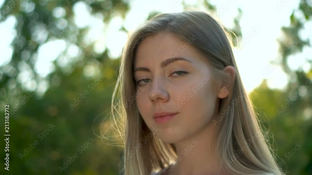 Wonderful young blonde woman with a lovely look and natural make up looking at camera smiling and running her hand through hair. Close up slow motion sunshine lens flare Wonderful young blonde woman with a lovely look and natural make up looking at camera smiling and running her hand through hair. Close up slow motion sunshine lens flare