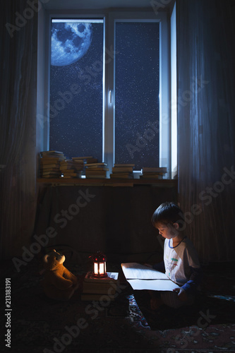 A boy sitting on the floor in the night light reading a book.