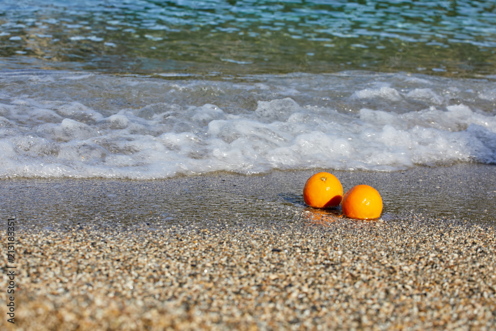 Naklejka premium Oranges lie on the sand. Waves from the sea are rolling ashore