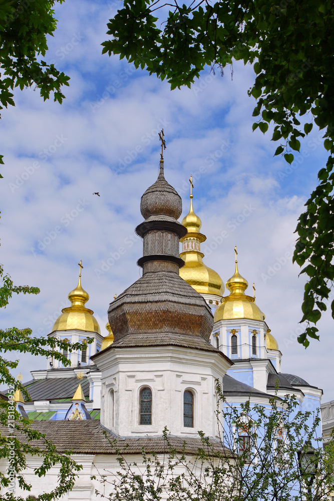 Ancient church with a wooden roof on the background of more modern temples with golden domes