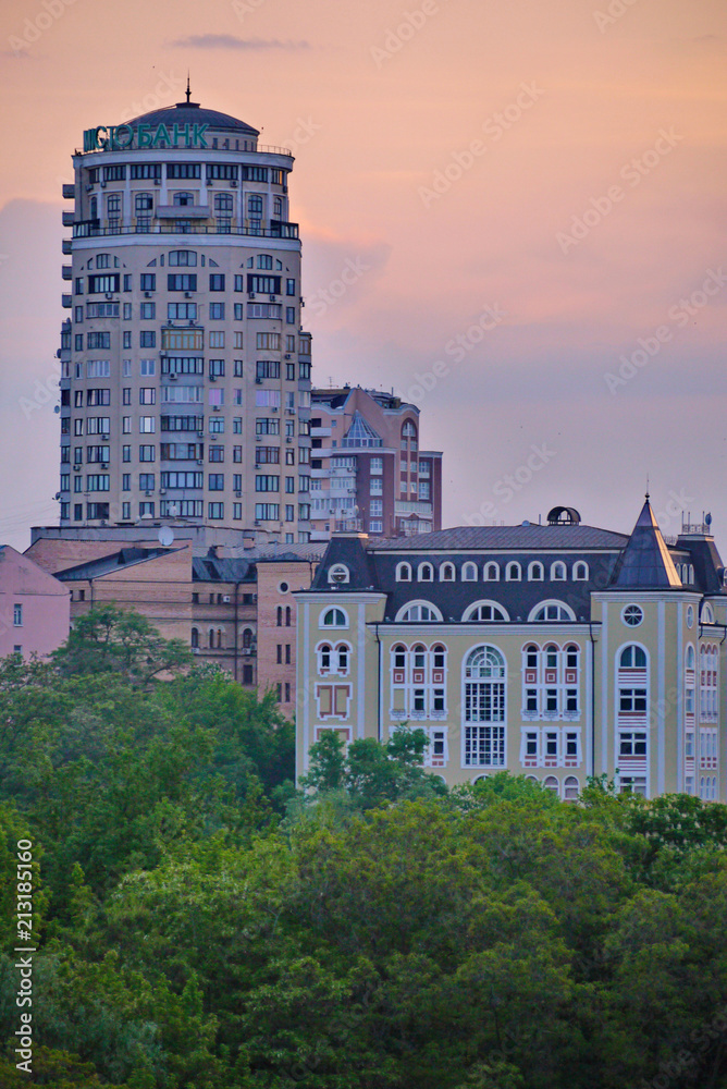 High urban high-rise buildings against the background of green trees and the evening sky
