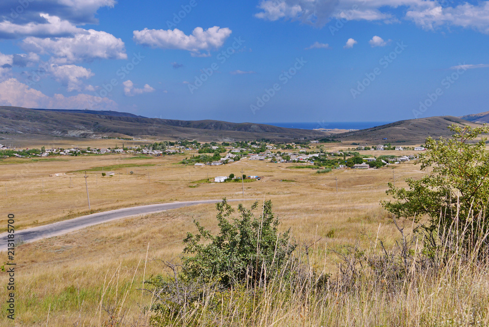 Outdoor landscape. Valley with a yellow dried grass and hills under a bright blue sky. And here is a small town Outdoor landscape. Valley with a yellow dried grass and hills under a bright blue sky. And here is a small town