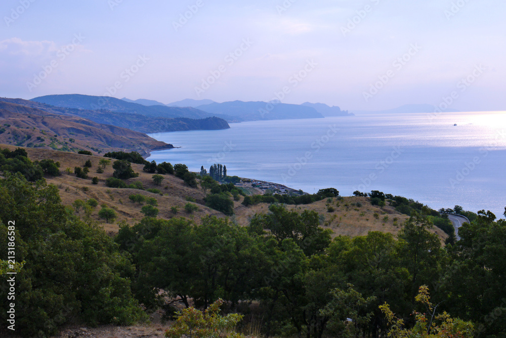 A calm sea bay with a coastal strip of stony hills reaching the water itself.