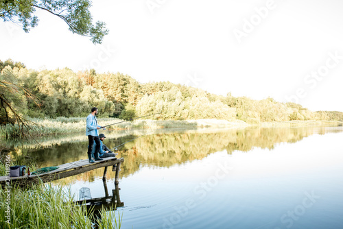 Two male friends fishing together standing on the wooden pier during the morning light on the beautiful lake