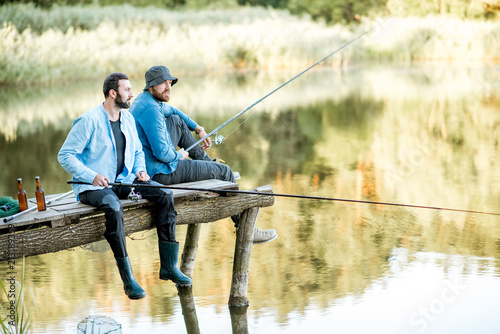 Dwaj męscy przyjaciele ubrani w niebieskie koszule łowią razem z siatką i wędką siedzącą na drewnianym molo podczas porannego światła na jeziorze