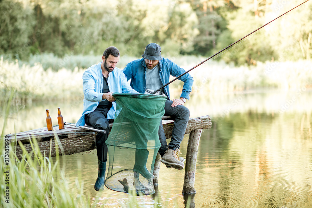 gidsel forklædt ekstremister Two happy male friends looking at the fishing net with fish during the  fishing on the lake Stock-foto | Adobe Stock