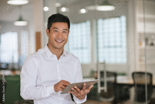Smiling Asian businessman using a digital tablet in an office