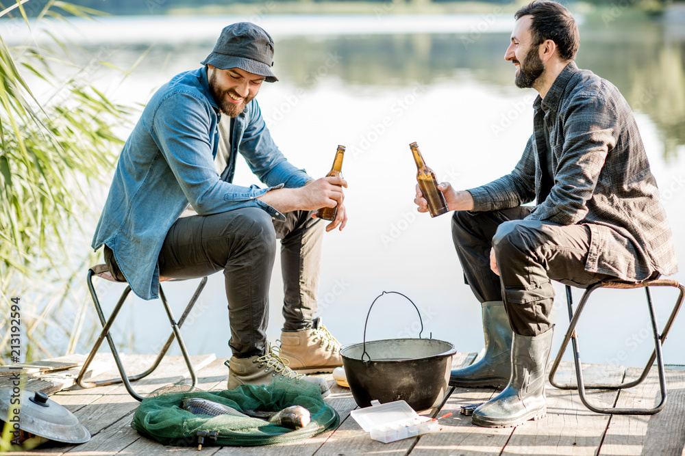 Two fishermen sitting together with beer while fishing on the lake at the morning