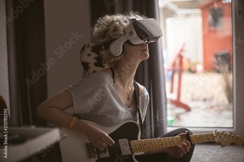 Young woman using virtual headset while playing guitar at home