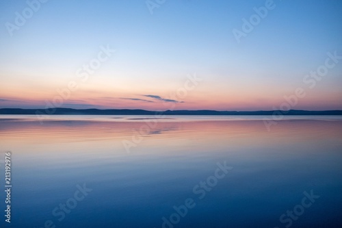 soft and calm sunset at Balaton lake in summer - thin clouds, velvet waves on water and hills in background