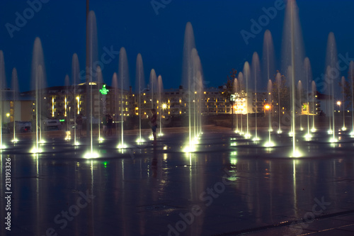 Les gens sous les jets d'eau de la fontaine à la tombé de nuit après une journée chaude, Espagne. 