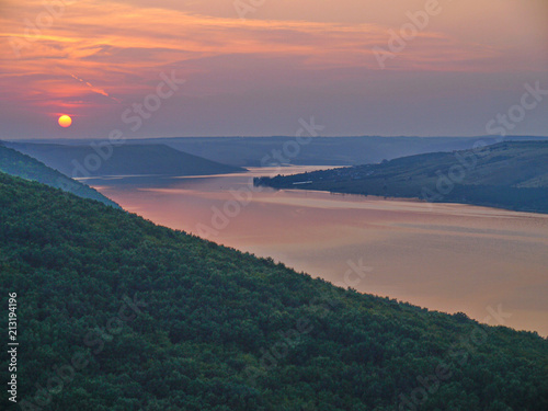 Fototapeta Naklejka Na Ścianę i Meble -  A picturesque view of the river bay in the middle of the green mountains against the evening sunset