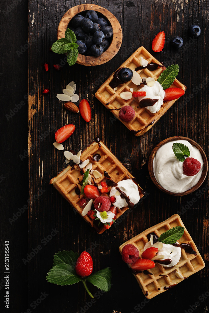 Waffles with berries on old black rustic background.