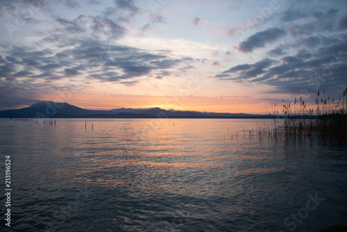 Fototapeta Naklejka Na Ścianę i Meble -  Sunrise on the lake. Early morning landscape. mountain in  silhouettes and the rays of the rising sun. Sunrise on Lake Garda, Italy