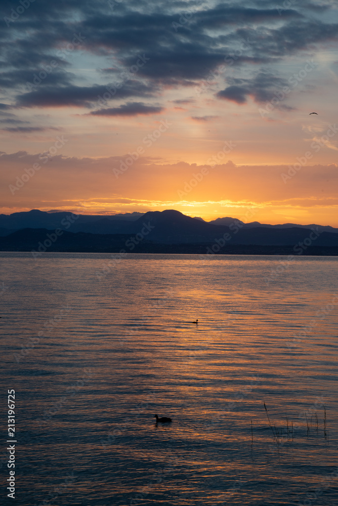 Sunrise on the lake. Early morning landscape. mountain in  silhouettes and the rays of the rising sun.Sunrise on Lake Garda, Italy.