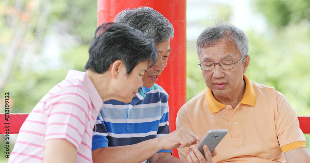 Senior friends talk together look at mobile phone at outdoor park Senior friends talk together look at mobile phone at outdoor park