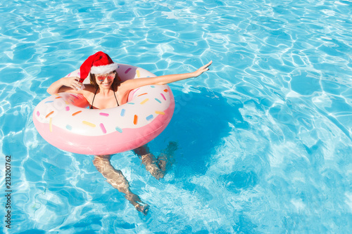 Beautiful happy woman in christmas hat with inflatable ring relaxing in blue swimming pool. copy space