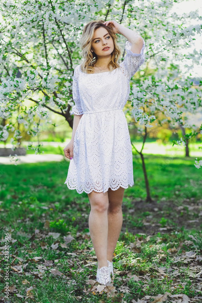 Beautiful blonde girl with blond hair in a dress on a background of spring blooming trees