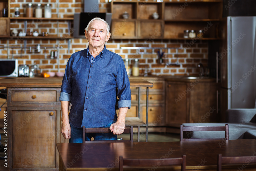 Serious elderly man standing in the kitchen Serious elderly man standing in the kitchen