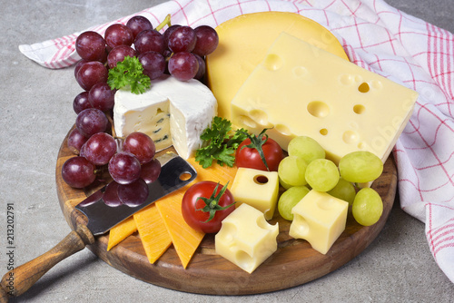 Delicious cheese plate with various sorts of cheese like Emmentaler, gouda and brie. Gourmet cheese on a wooden cutting board with white concrete background and kitchen towel.