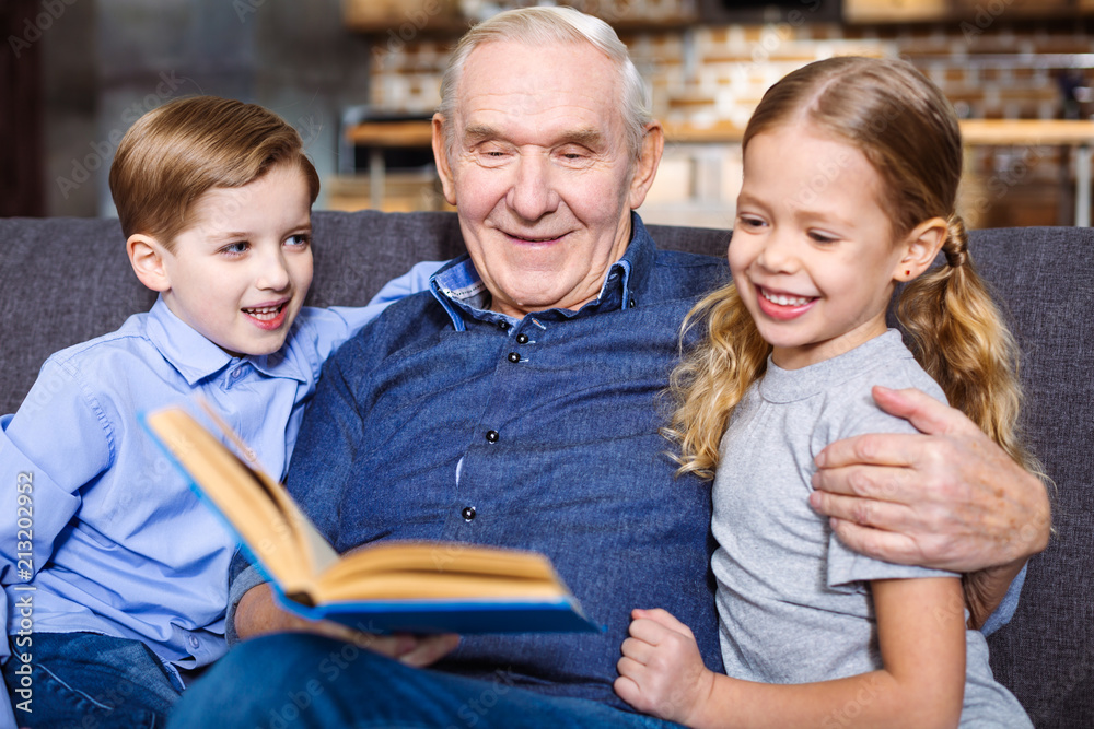 Waist up of cheerful elderly man reading for his grandchildren Waist up of cheerful elderly man reading for his grandchildren