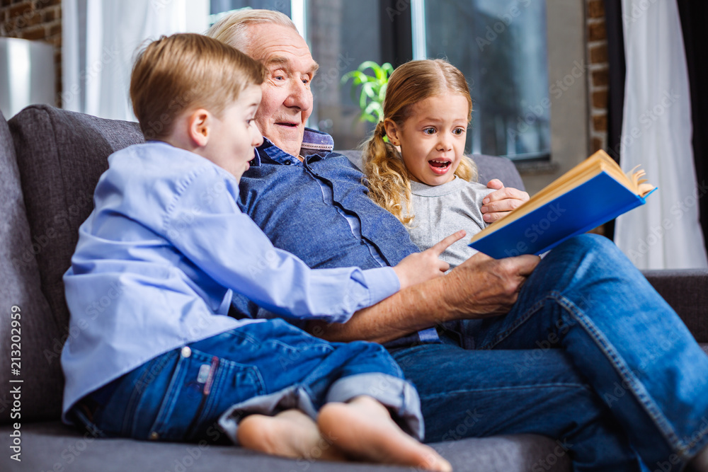 Positive little siblings reading a book with their grandfather