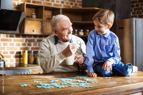 Positive aged man assembling jigsaw puzzle
