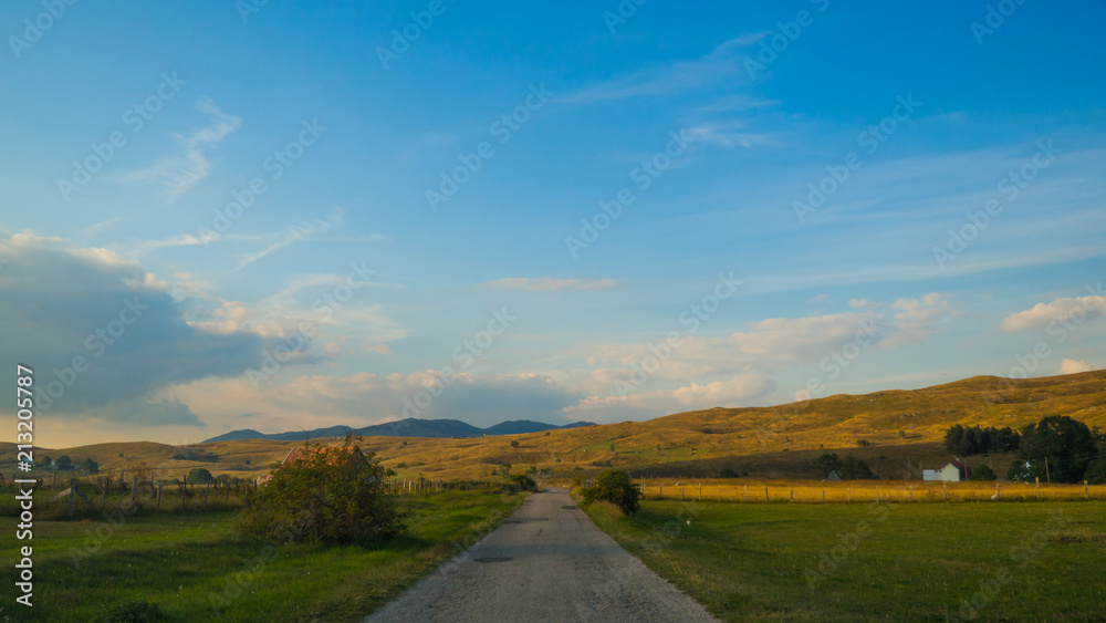 Movement on the road in the countryside in the evening with yellow meadows on the sides and pretty village houses