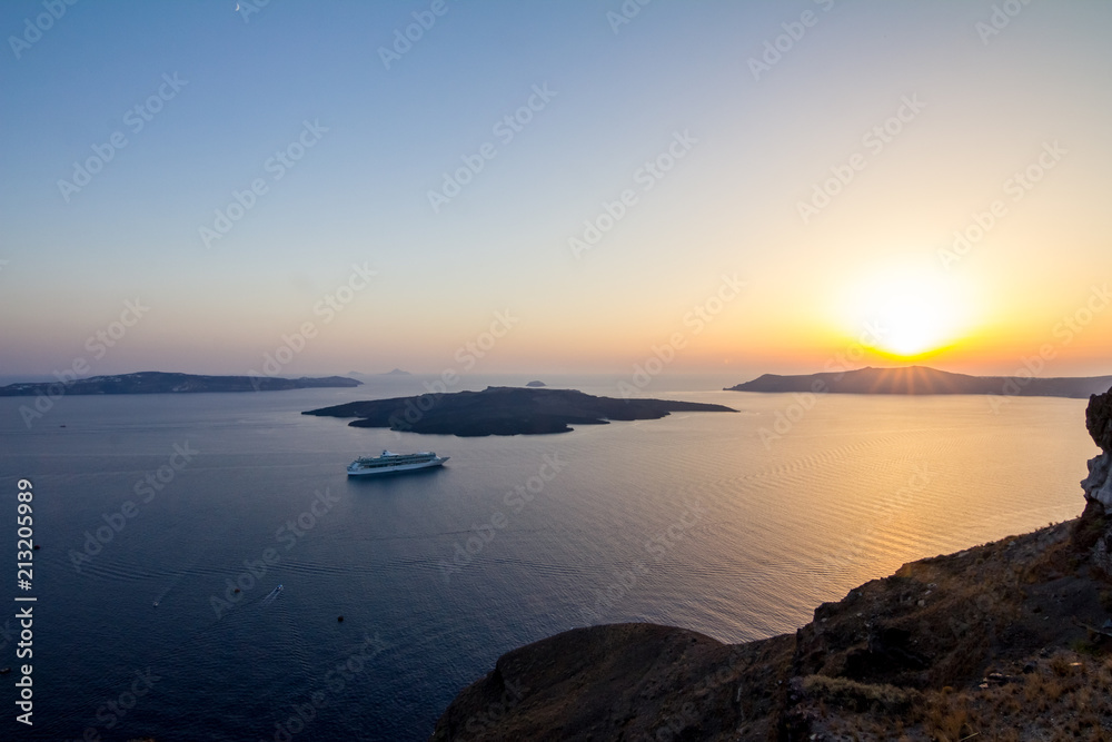 Elevated incredibly romantic sunset scene on Santorini. Fira, Greece, from above. Amazing golden hour view from public path walk towards volcano in the center of the caldera. Shortly before the sunset