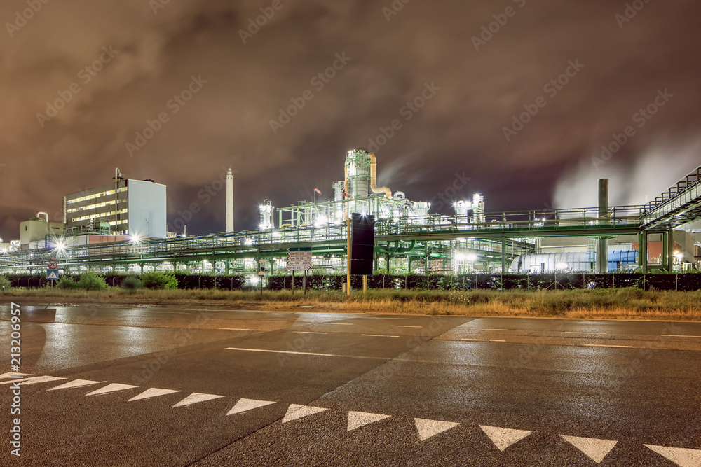 Illuminated petrochemical production plant against a cloudy blue sky at night, Antwerp, Belgium.