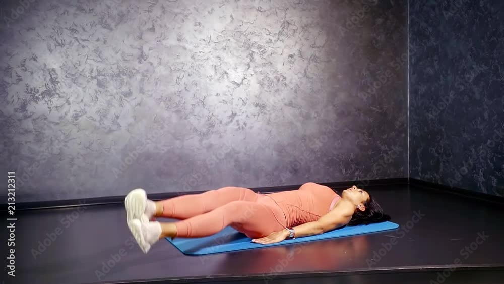 girl trainer in a comfortable sports suit shows the allocation of direct exercise of the legs in side lying on back