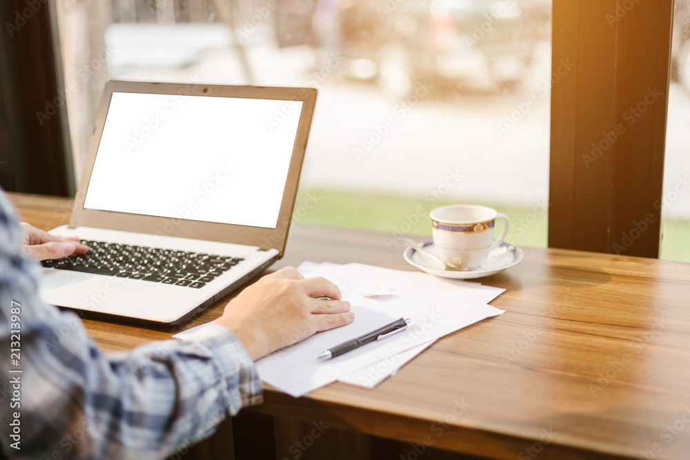 Close-up of businessman working with laptop with blank white screen,smart phone and document on in coffee shop like the background. Close-up of businessman working with laptop with blank white screen,smart phone and document on in coffee shop like the background.