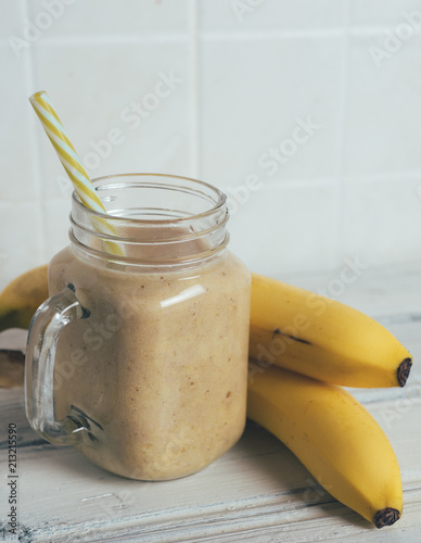 Freshly ground yellow banana smoothie cocktail in a mug on a white wooden table