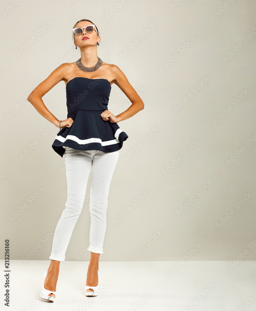 Fototapeta premium Beautiful and attractive model dressed in expensive clothes. White pants, navy blue blouse and high heels. A photo of a fashion shot in the studio.