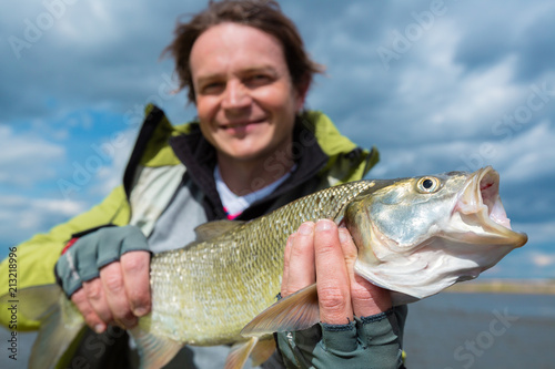 Young amateur angler hold the Asp fish (Aspius aspius) with lake on the background. Focus on the fish head