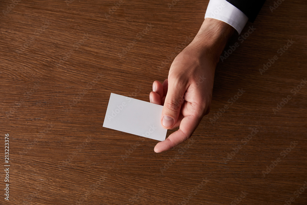 cropped image of businessman giving blank business card at wooden table cropped image of businessman giving blank business card at wooden table