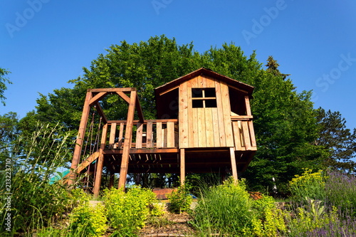 Beautiful DIY wooden playhouse for children with swing and slide on a hillside in a sunny day photo