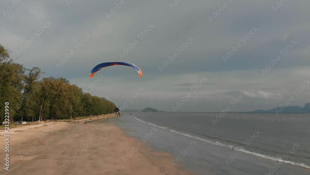 Para motor flies along the sandy beach over the sea. Background with islands view. The coast of Thailand. Trang province. Sikao. Paraglide. Paramotor. Para motor flies along the sandy beach over the sea. Background with islands view. The coast of Thailand. Trang province. Sikao. Paraglide. Paramotor.
