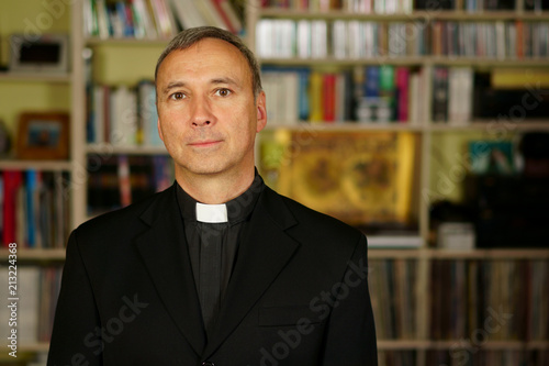 A portrait of a good looking serious catholic priest.  He looks at us with interest, pensiveness, proselytising, joy, happiness, trust and peacefulness.