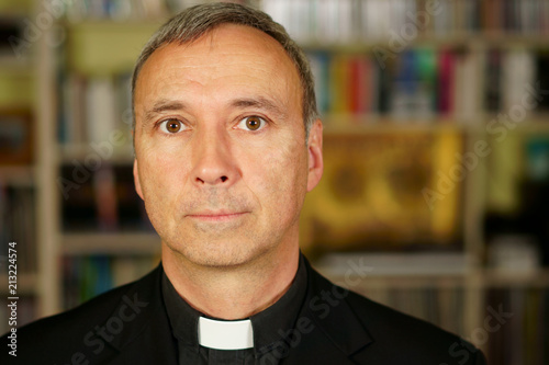 A portrait of a good looking serious catholic priest.  He looks at us with interest, pensiveness, proselytising, joy, happiness, trust and peacefulness. photo