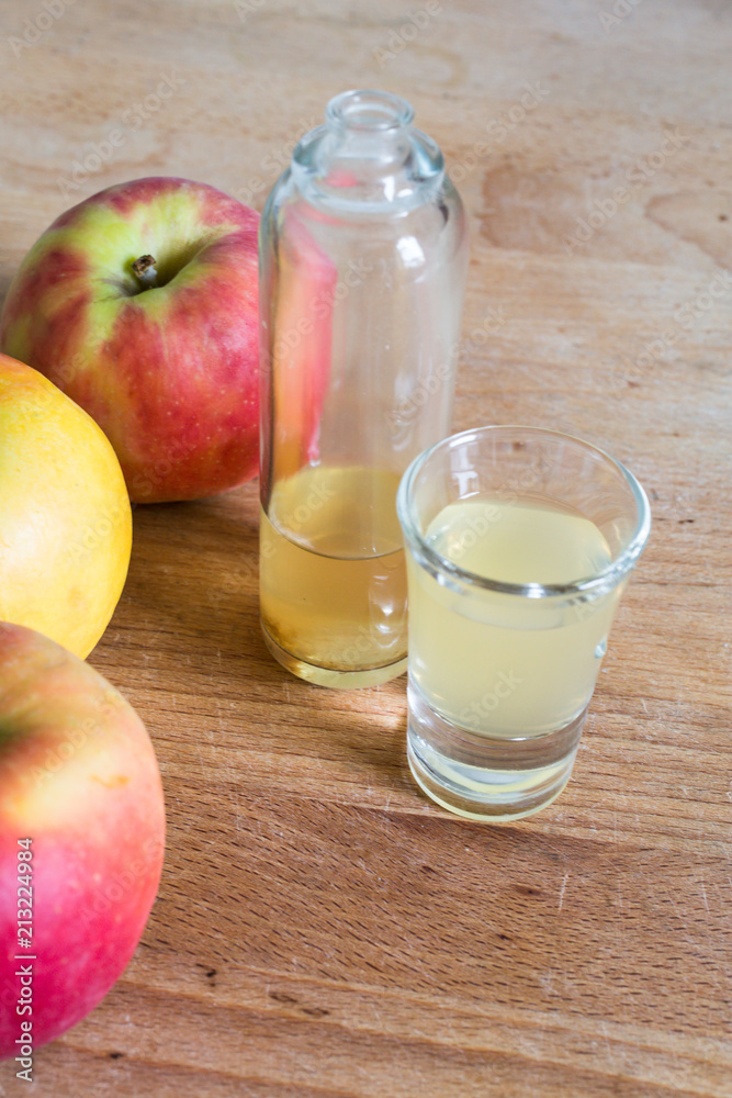 portrait of bottle and glass filled with naturally cloudy apple cider vinegar with apples as decoration on wooden table