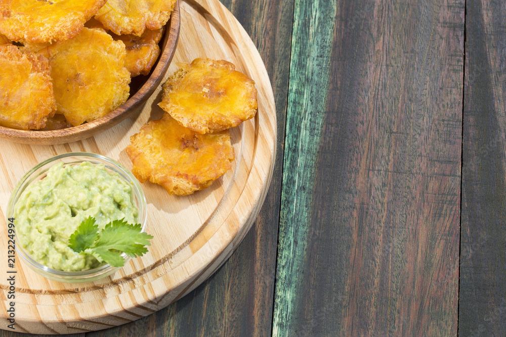 Patacon fried pieces of crushed green banana. Guacamole. On the wooden table (toston, tachino)