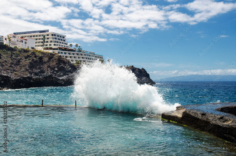 Big ocean wave breaking on the natural outdoor swimming pool in the resort town of Los Gigantes (