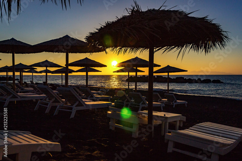 Sun beds during sunrise on beach of Kamari, Santorini, Greece