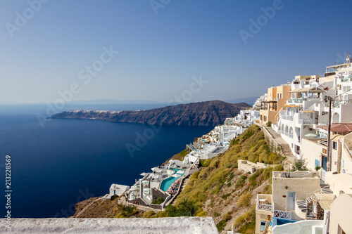 Fototapeta Naklejka Na Ścianę i Meble -  Terrace with view, incredibly romantic scene, Santorini. Fira, Greece. Amazing daytime cityscape towards Oia and the deep sea crystal waters with white houses and swimming pools