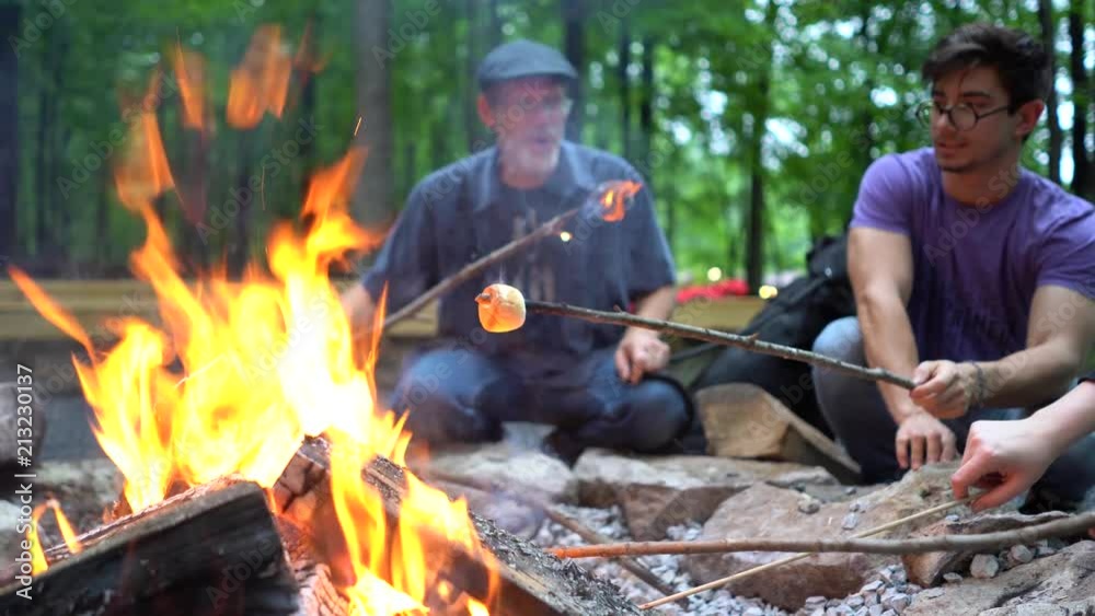 Low angle focus shift from marshmallows over fire to a man blowing out a marshmallow on fire. Low angle focus shift from marshmallows over fire to a man blowing out a marshmallow on fire.